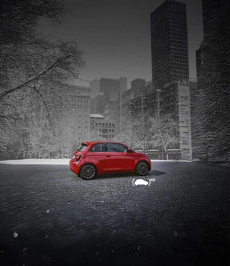 A red Fiat 500e Red parked on a city street in winter, with snow blanketing the trees and everything presented in black and white except the vehicle.