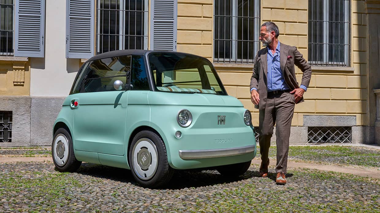 A mint green Fiat Topolino parked at a residential building, with a man standing next to it.